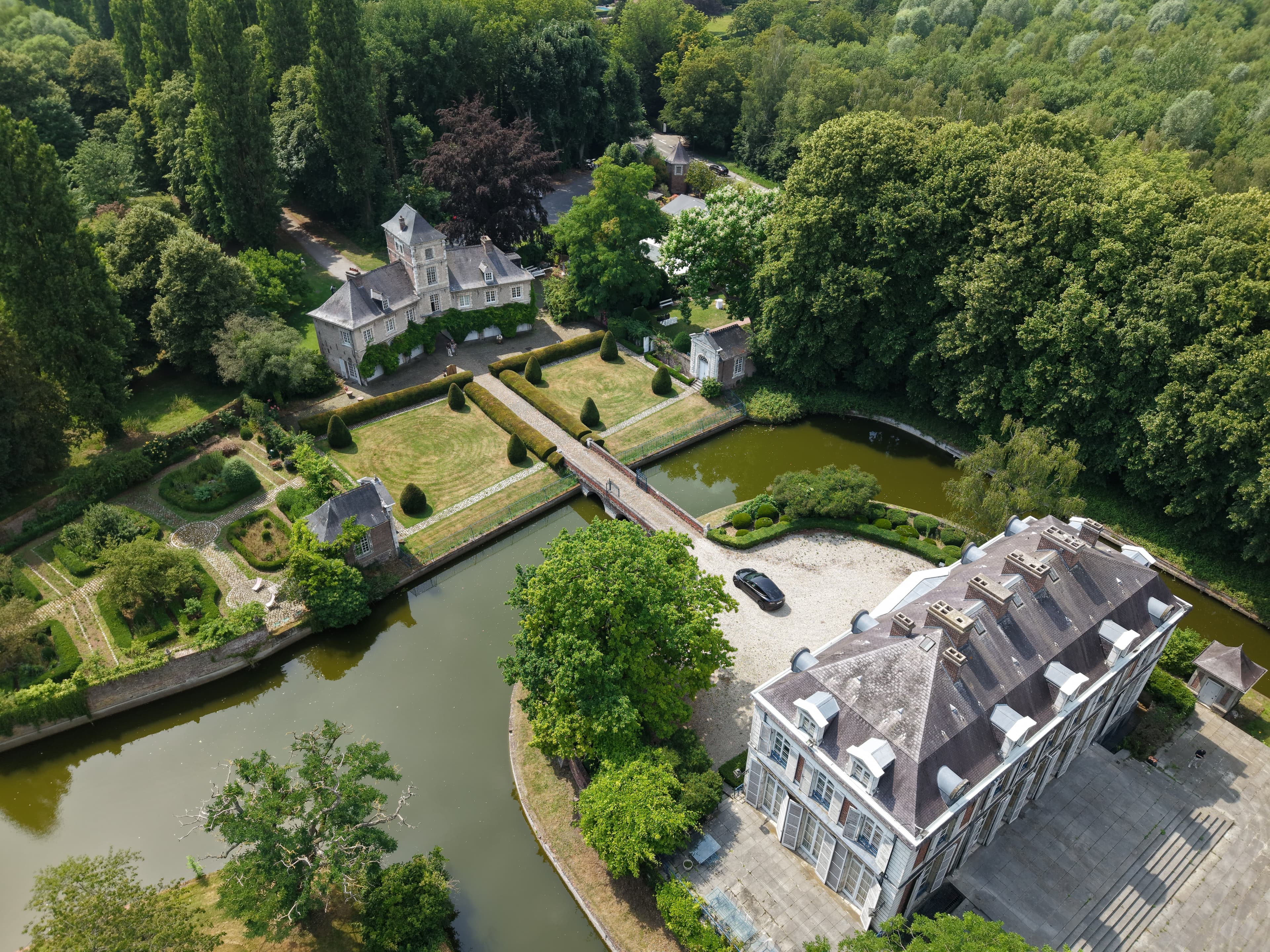 Vue aérienne d'un château entouré de douves, jardins et bois